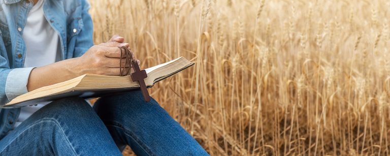 Christian Woman Praying On Holy Bible And Wooden Cross In Barley